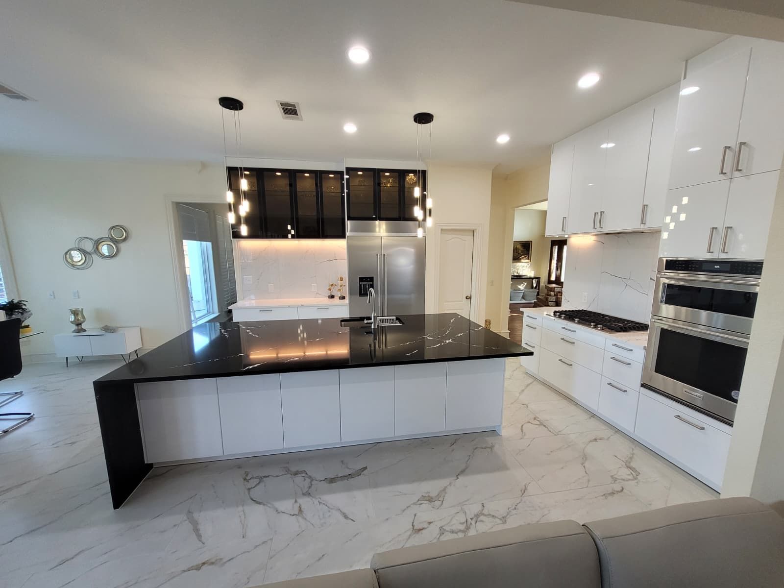 Modern kitchen with high-gloss white cabinetry, black glass display cabinets and a large black waterfall island installed by D&L Excellence Services in Central Florida